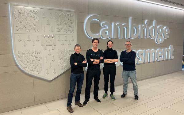 Colleagues pose in front of the Cambridge logo